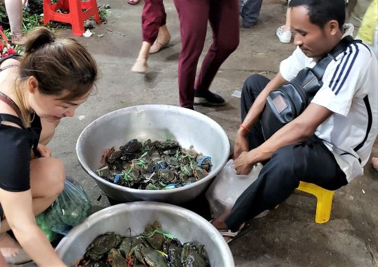 As visitors stroll through Sihanoukville's market in Cambodia, vendors seated on the floor within the aisle sell from tubs holding live fresh fish or crabs. Photo by Susan J. Young. 